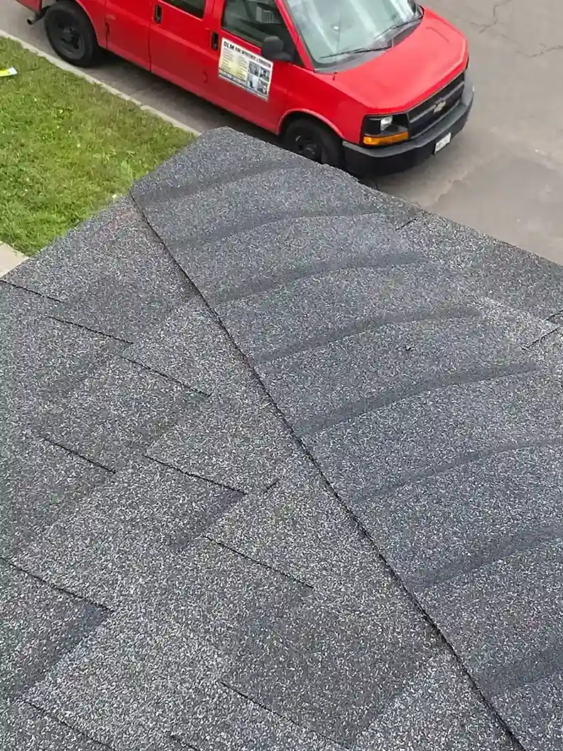 High-angle shot of a newly installed gray asphalt shingle roof with a red DLM Roofing service van parked on the street below.